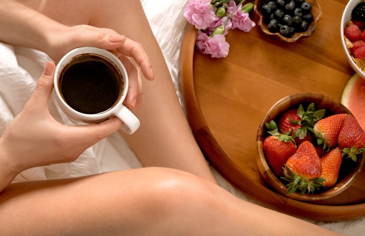Woman eating breakfast and drinks coffee in the bed.