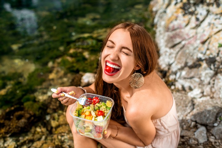 Woman eating healthy salad near the river